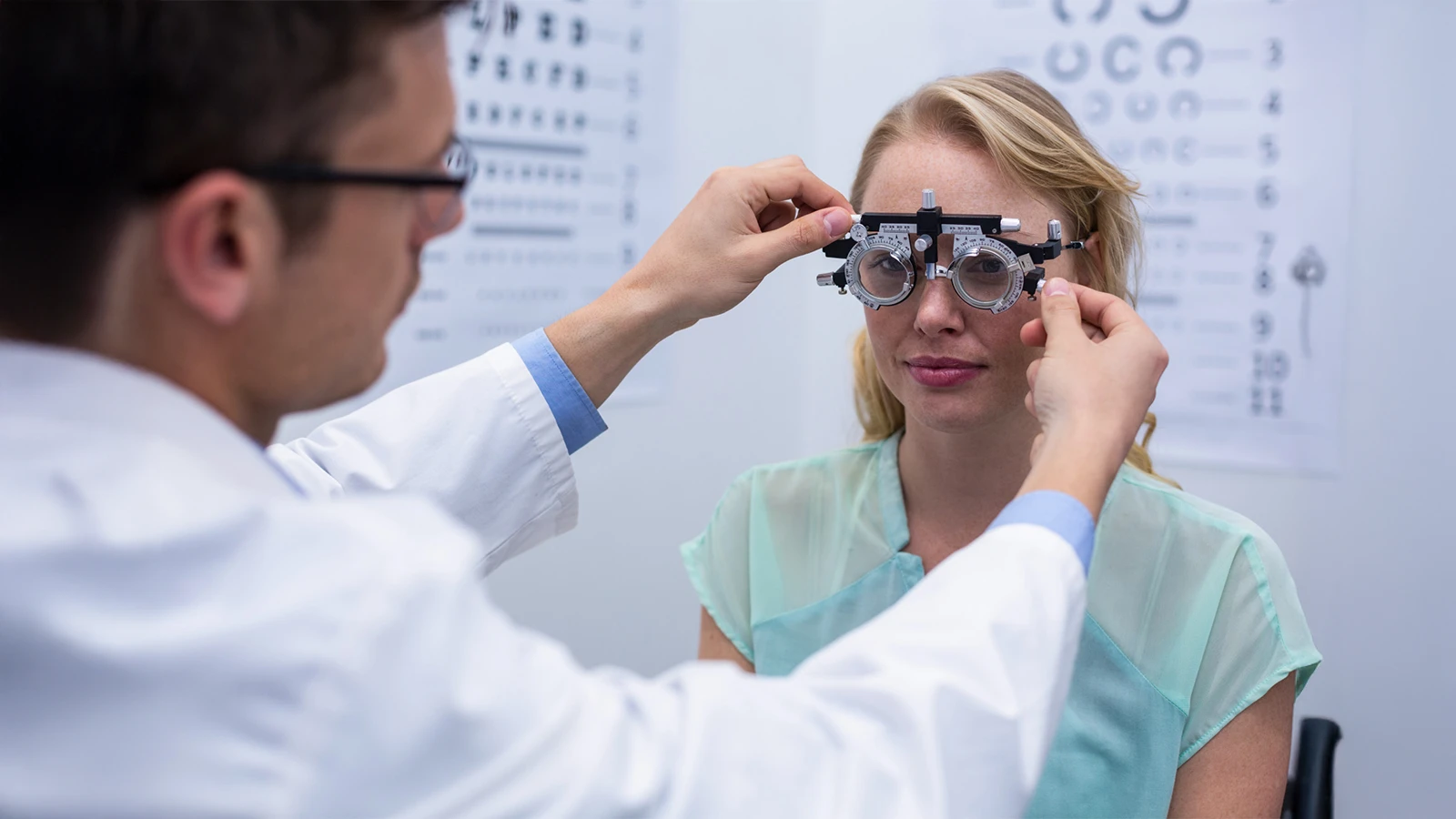 An optometrist adjusts a phoropter on a female patient during an eye examination to accurately determine the correct prescription power for her glasses.
