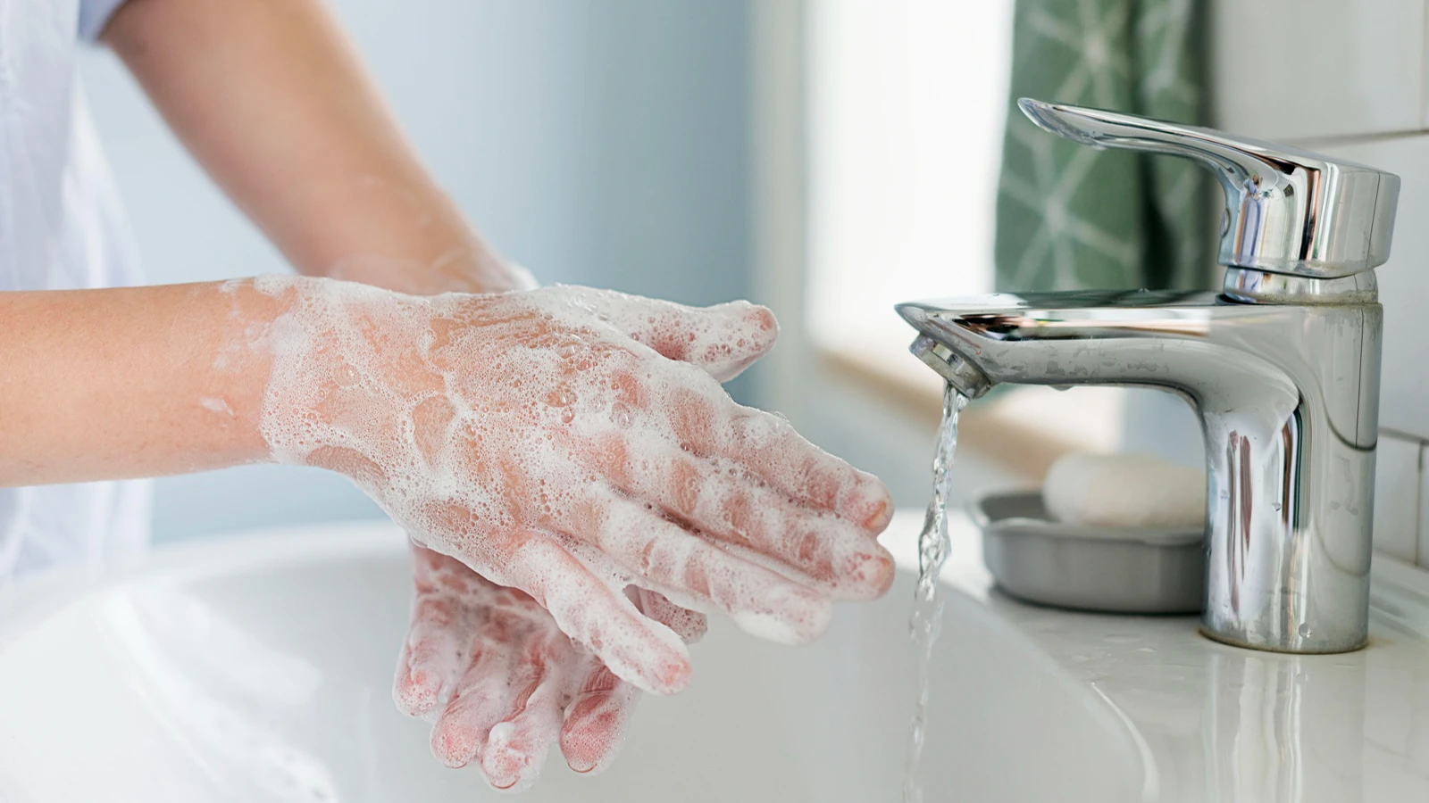 Lathering hands with white soap suds over a white sink with water running from a chrome faucet.